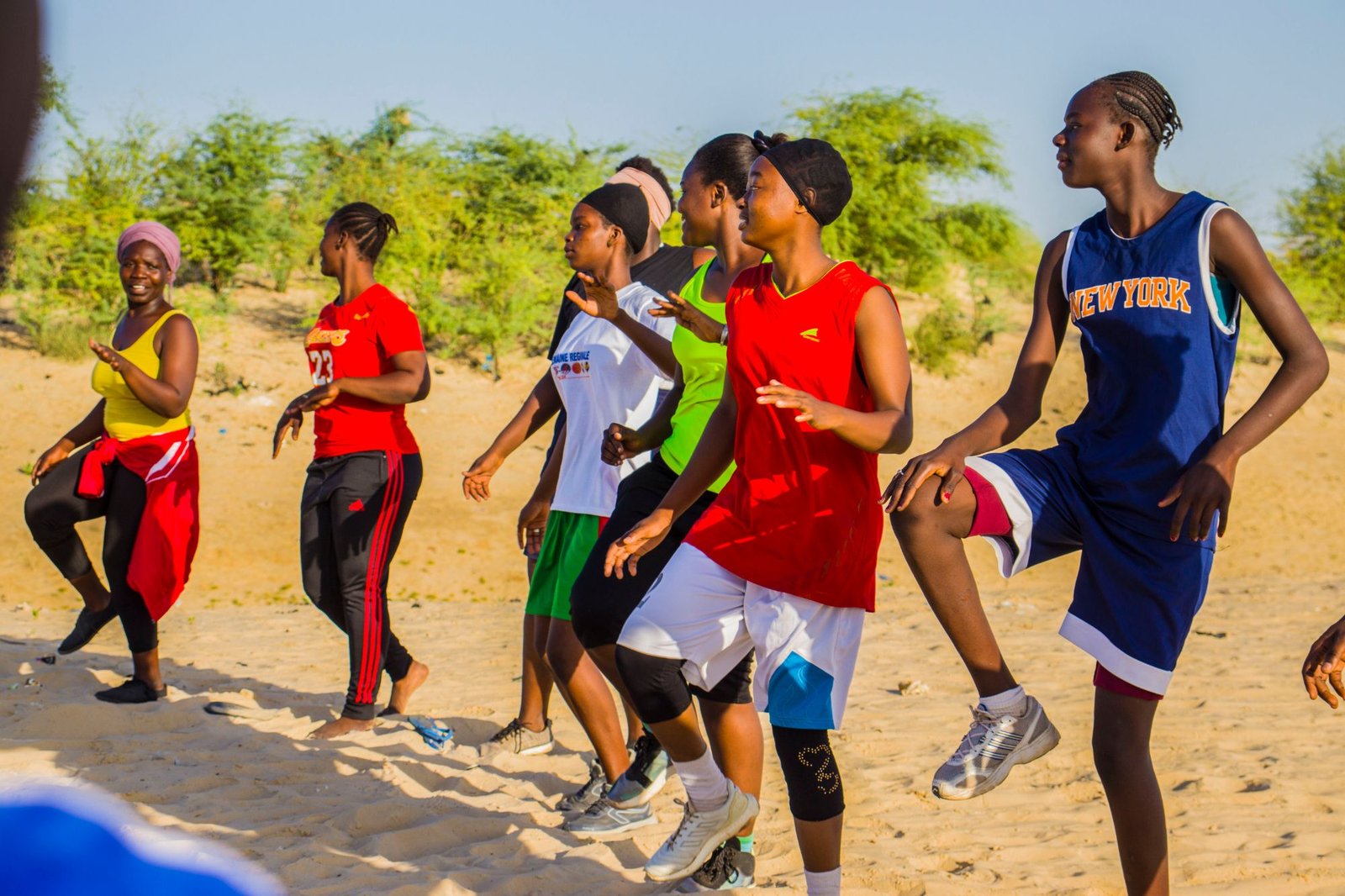 Un groupe de jeunes en tenue de sport réalise un exercice collectif sur un terrain de sable.
