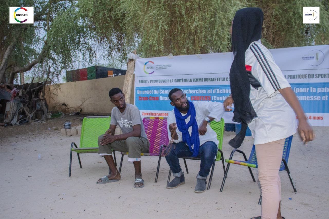 Une table ronde se tient en plein air devant la banderole du projet.